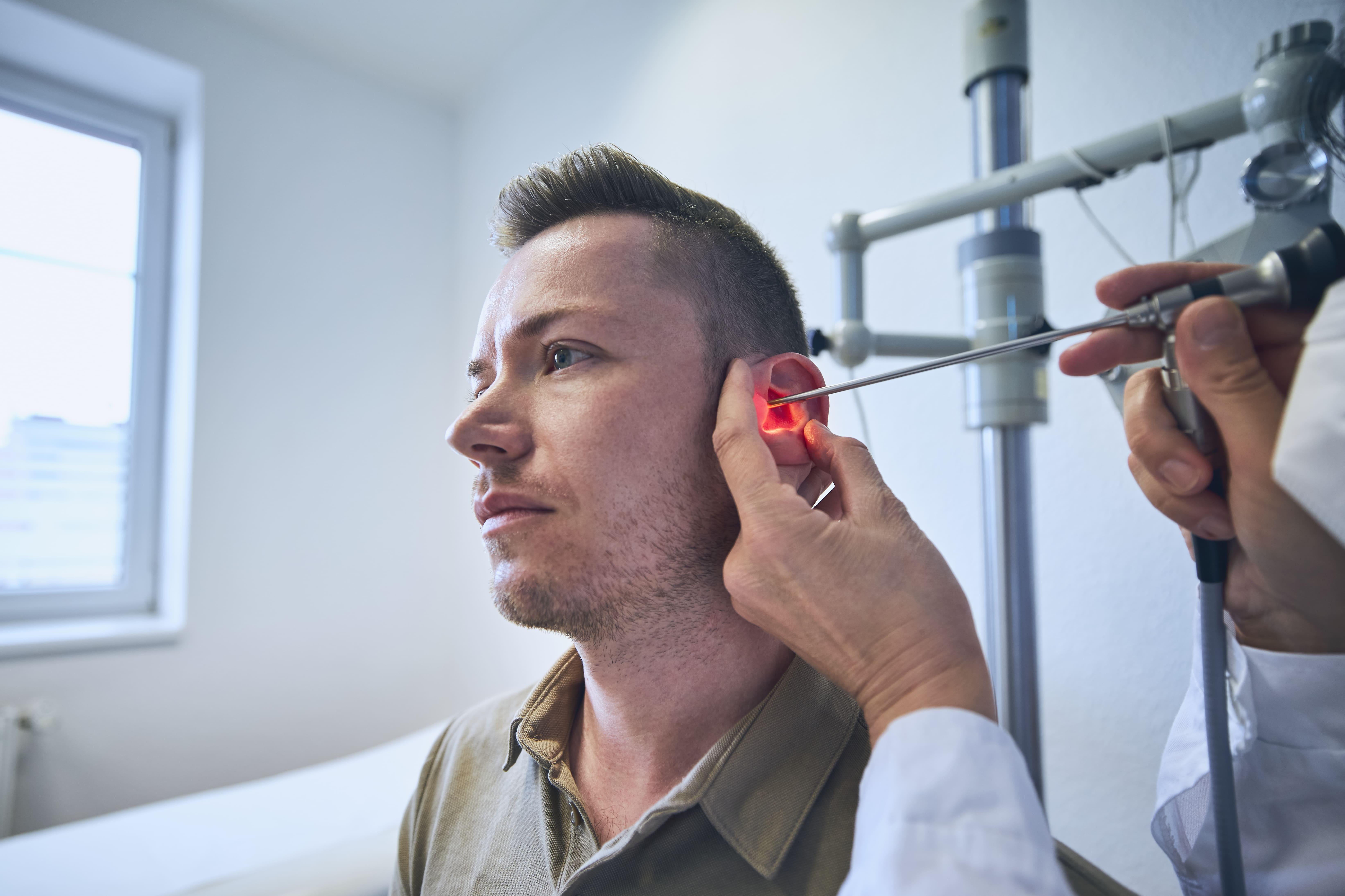 Especialista usando un otoscopio iluminado para realizar una extracción de tapones de cerumen en un paciente