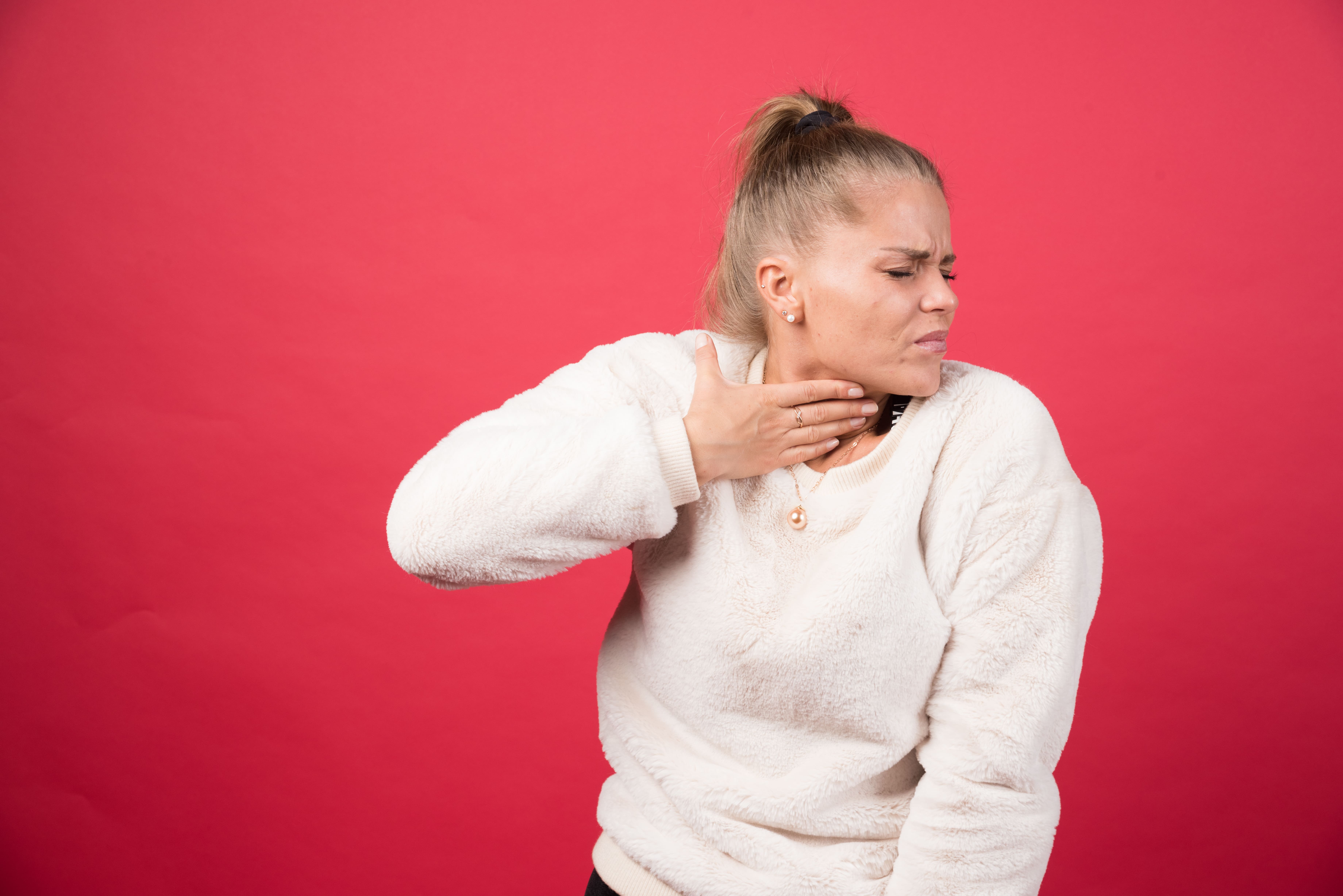 Afonía. Síntomas y tratamiento en Madrid - Mujer joven rubia tocándose la garganta con dolor mostrando síntomas típicos de afonía