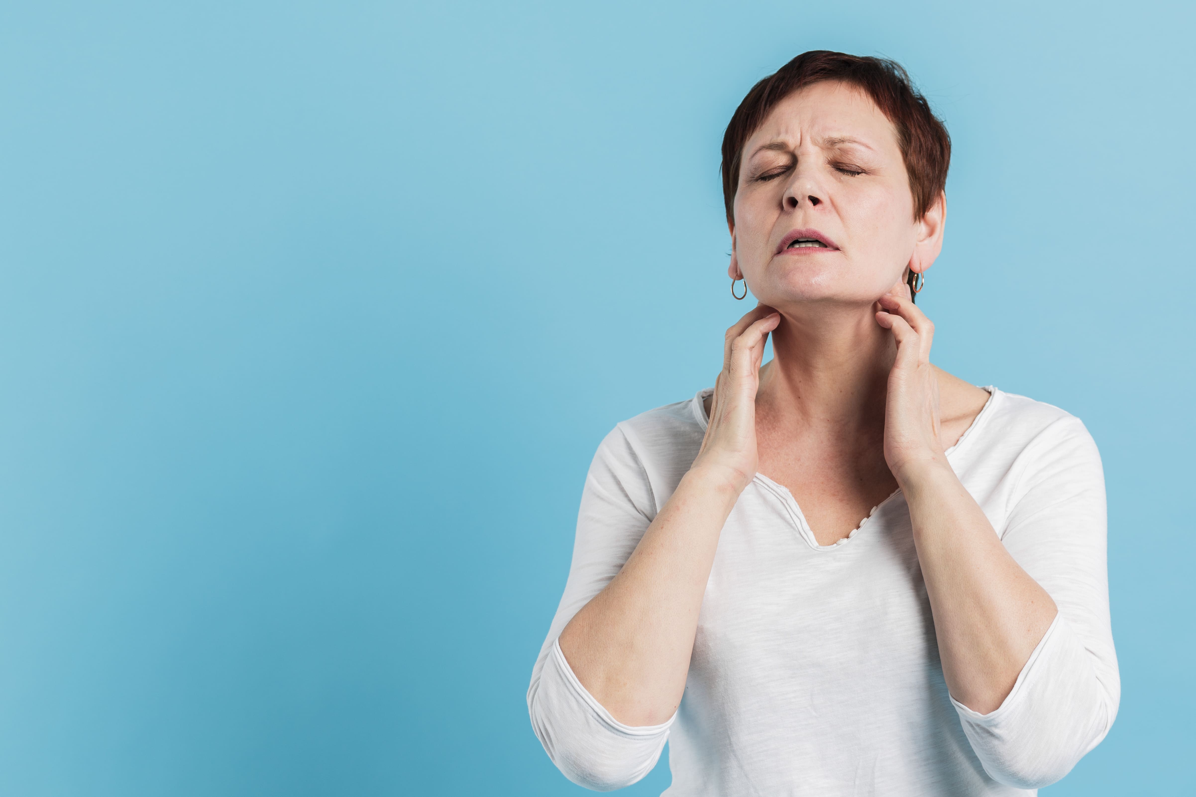 Disfonía. Síntomas y tratamiento en Arganda del Rey - Mujer de mediana edad tocándose la garganta con dolor mostrando síntomas de disfonía