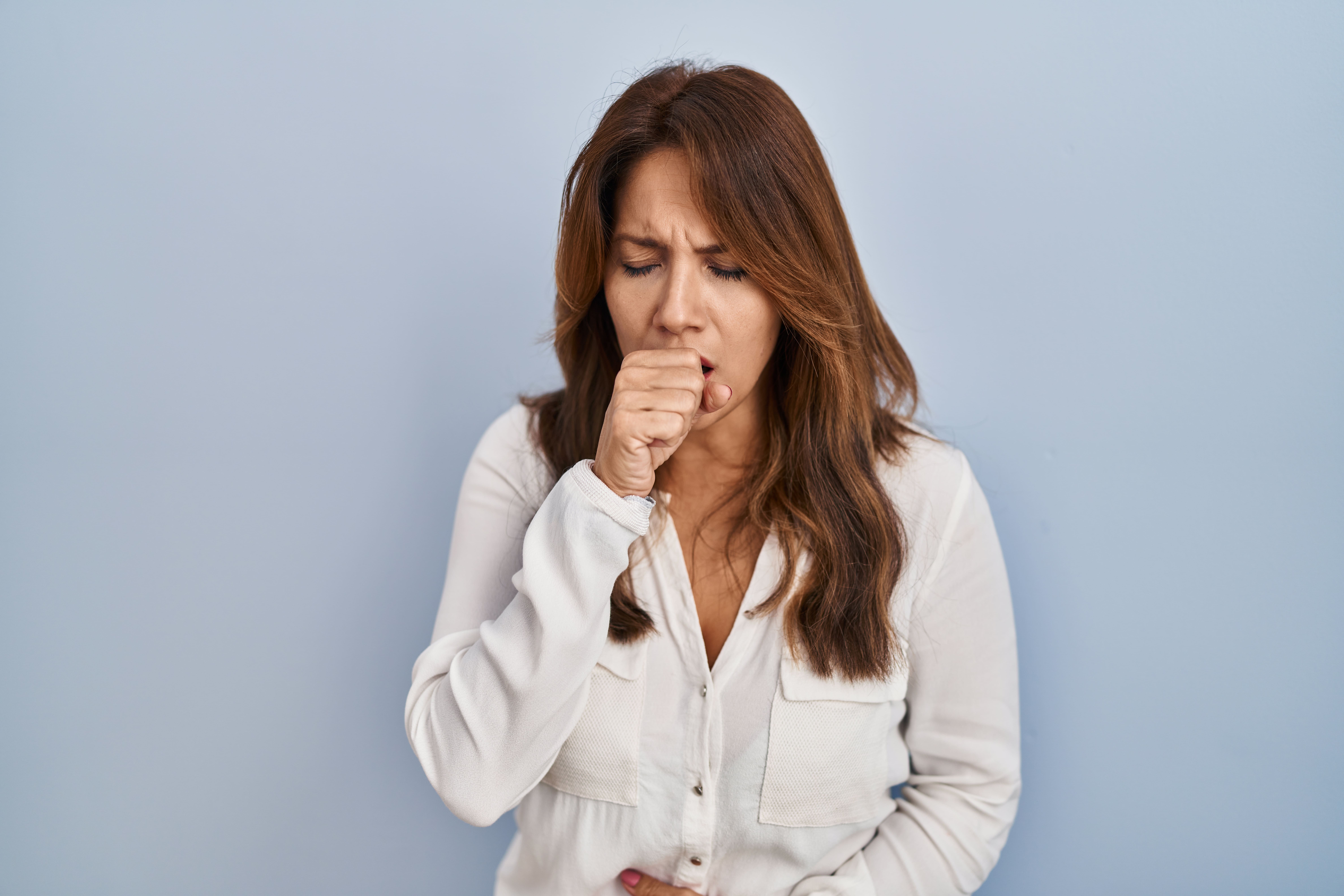Mujer con expresión de dolor mientras tose fuertemente, posible caso de bronquitis.