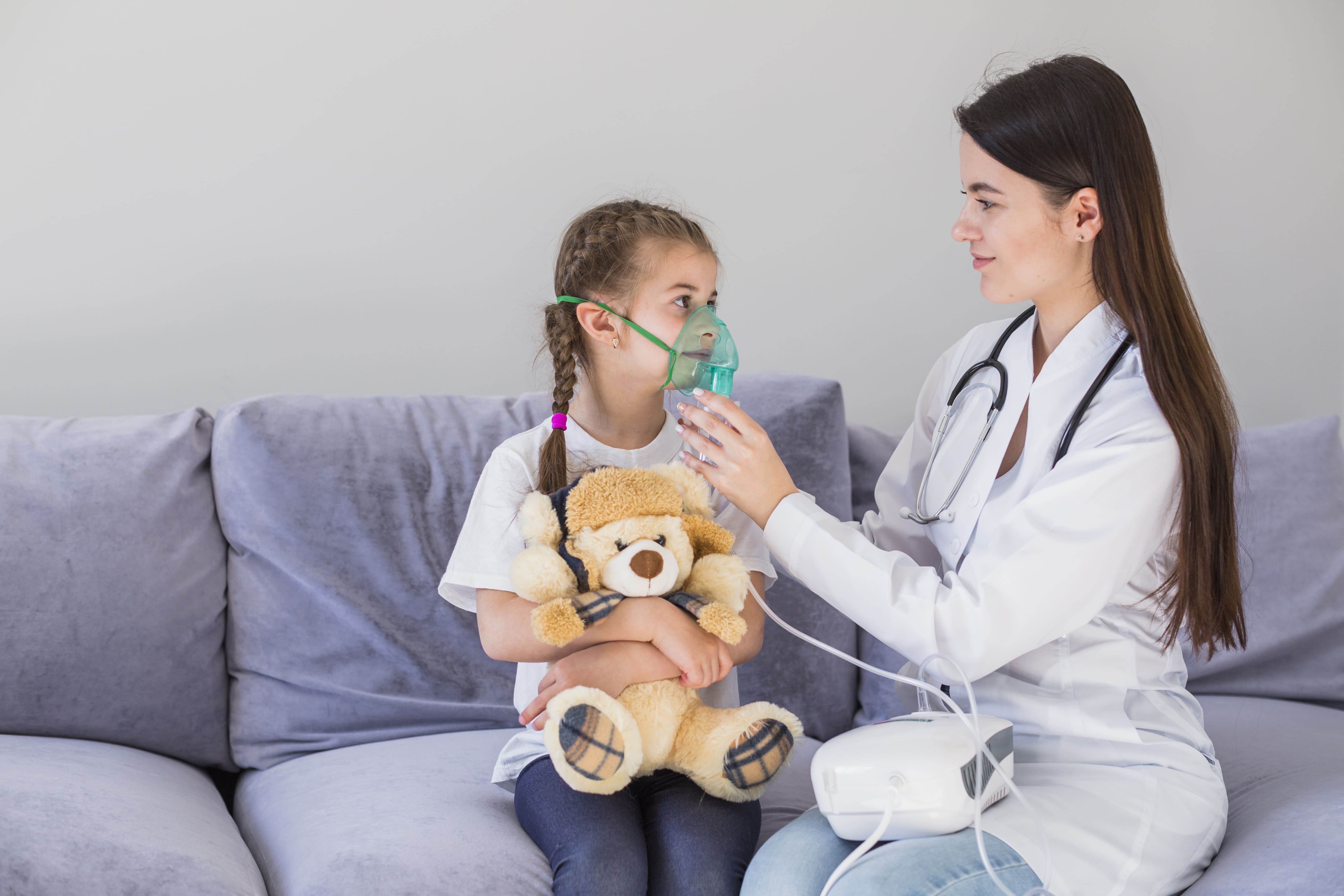 Niña recibiendo fisioterapia respiratoria infantil en [Keyword] con nebulizador y acompañada de una profesional sanitaria.